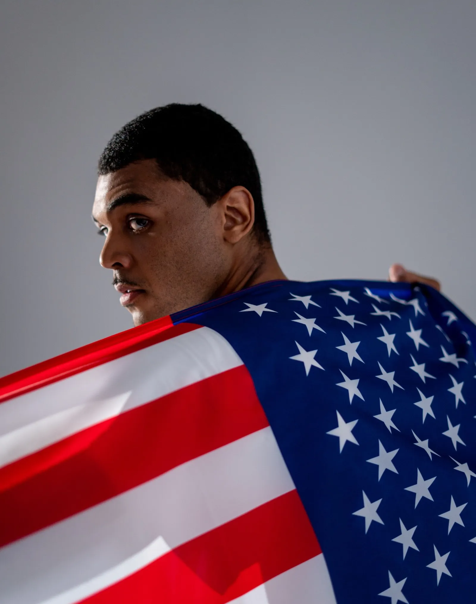 A young man looks over his shoulder while holding an American flag across his back.