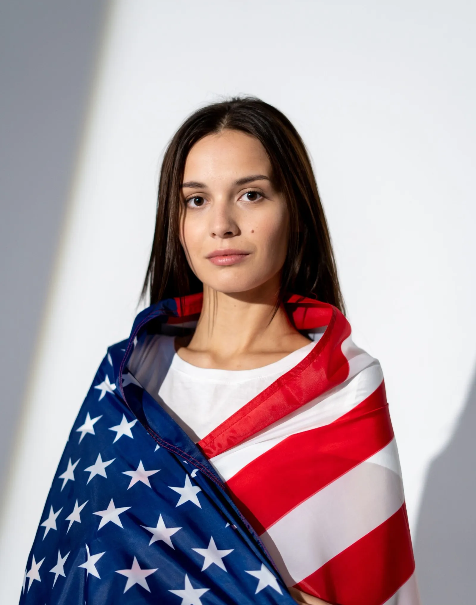 A young woman wrapped in an American flag looks at the camera.